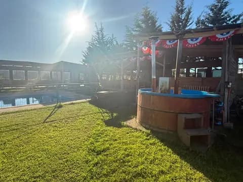 Tinaja de agua caliente al aire libre rodeada de áreas verdes, junto a la piscina